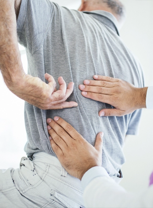 Close-up of hands placed on a person’s lower back while receiving a back adjustment in a clinical setting.