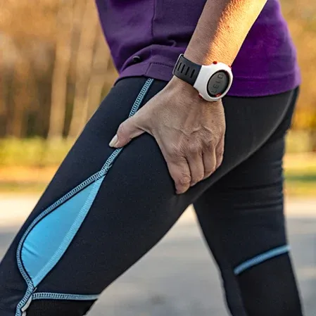 Close-up of a person holding the upper thigh while wearing athletic leggings and a fitness watch.